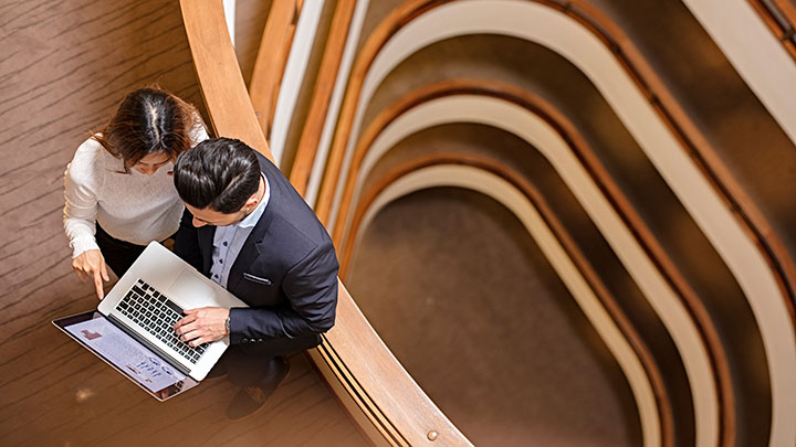 Zwei Geschäftsleute, die im Bürogebäude stehen und Laptops nutzen