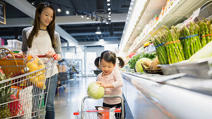 Jong meisje dat groenten koopt met haar moeder