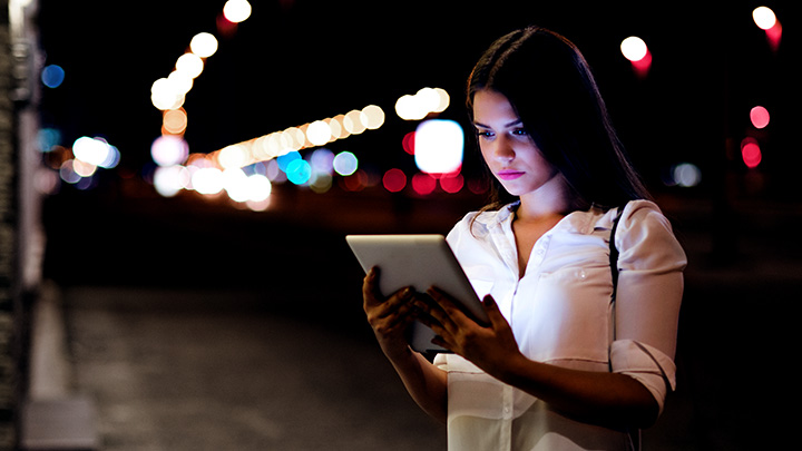 Woman looking at tablet on city street at night