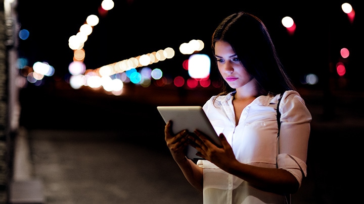 Vrouw in een straat die in de avond op een tablet kijkt