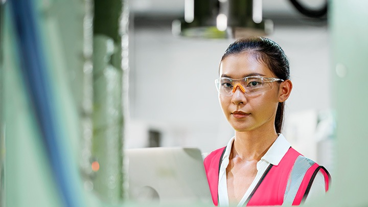 Female production engineer holding a laptop in front of automated steel press machine