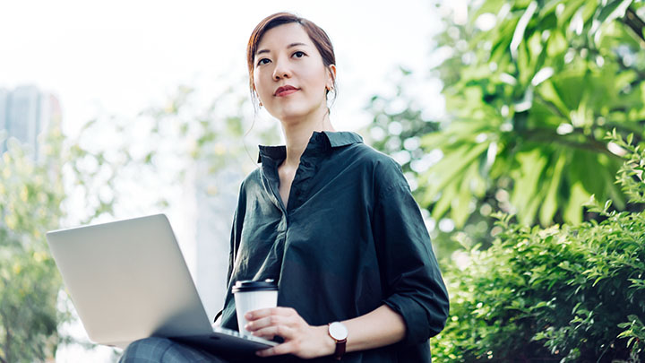 Femme d'affaires asiatique assise sur le banc et travaillant sur un ordinateur portable