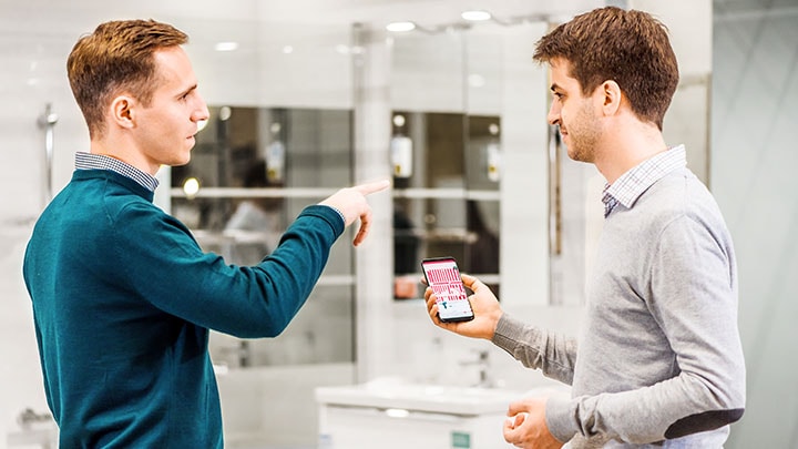 Twee mannen die de plaatsing van een product in een winkel bespreken met smartphonenavigatie