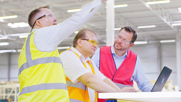 Three production managers discussing lighting on laptop in factory