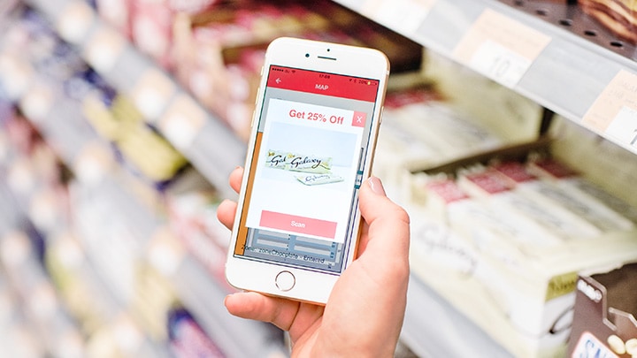 Una mujer en un supermercado, con una promoción lado de pasillo en la pantalla de su teléfono inteligente