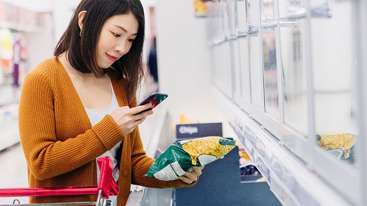 Una mujer asiática hace una compra de alimentos congelados con su teléfono inteligente en una tienda de comestibles