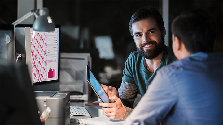 Twee mannelijke collega's die werk bespreken op een computer en tablet