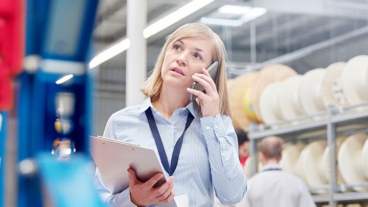 Female supervisor with clipboard talking on smart phone in factory