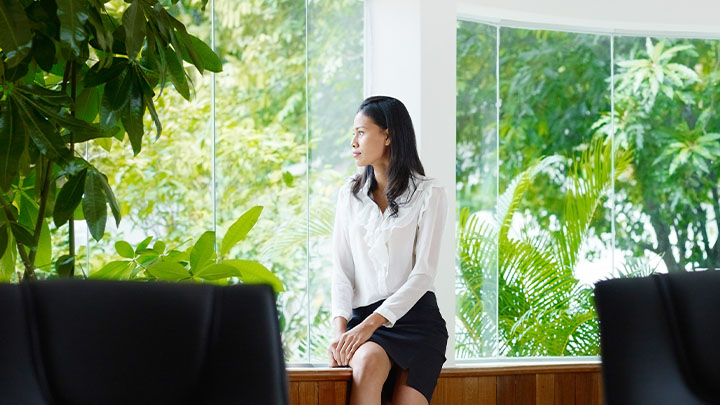 Une femme regardant un paysage naturel verdoyant depuis un bâtiment en verre moderne