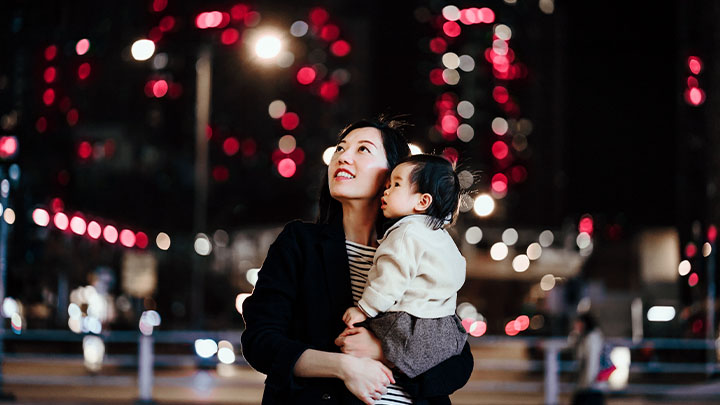 A woman holding her child, looking up at the city lights at night