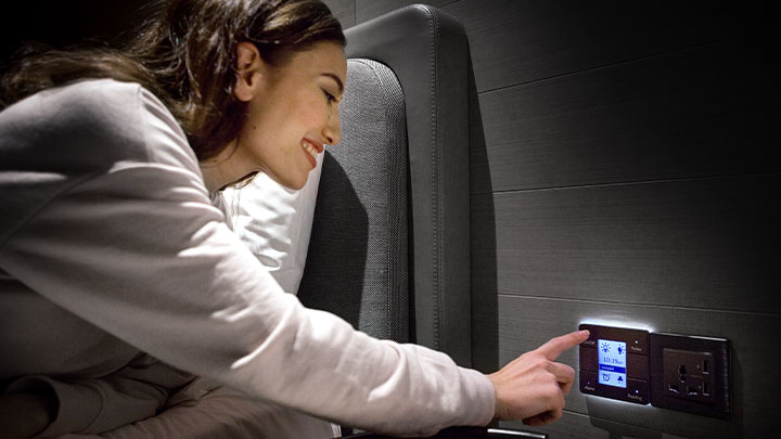 A woman in a hotel bed, reaching around to control a smart light switch