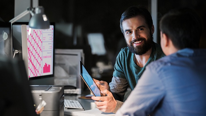 Two workers in an office talking to each other over a tablet