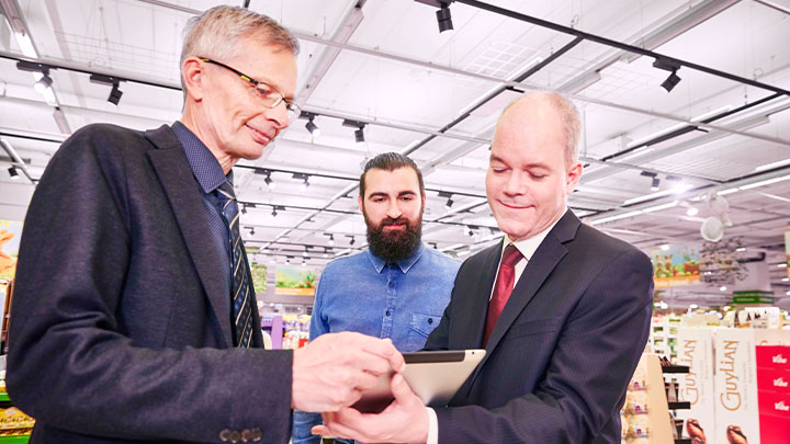 Trois gérants d'un supermarché regardent tous une tablette en souriant