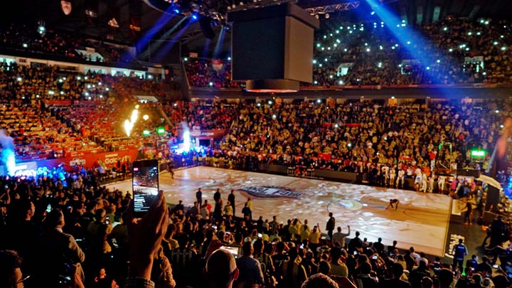 The interior of a busy basketball stadium with colourful lighting