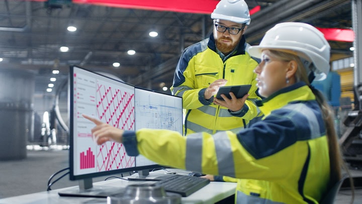 Two workers in high visibility jackets talking over a computer in a warehouse