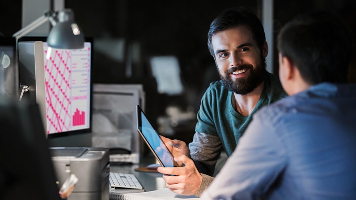 Two workers at their desks, in an office at night, talking to each other