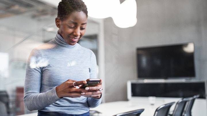 Een vrouw in een lege vergaderruimte op kantoor, die naar haar telefoon kijkt en glimlacht