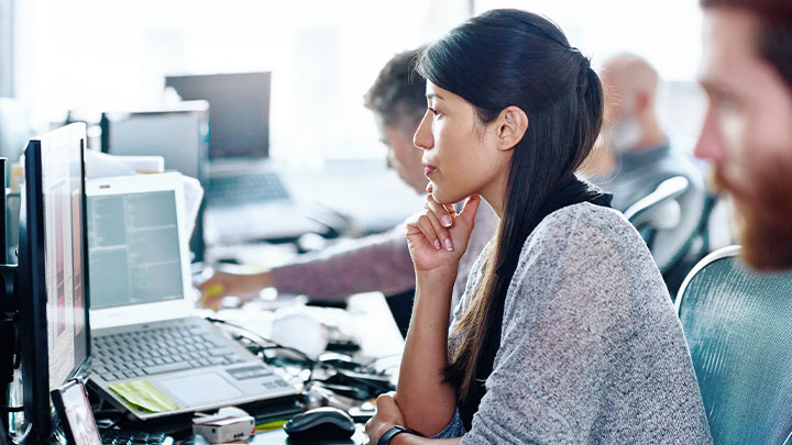 Een medewerker die geconcentreerd naar haar computerscherm kijkt in een druk kantoor