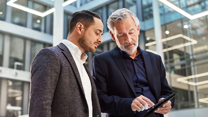 Two colleagues in a wide open Office foyer looking at a tablet