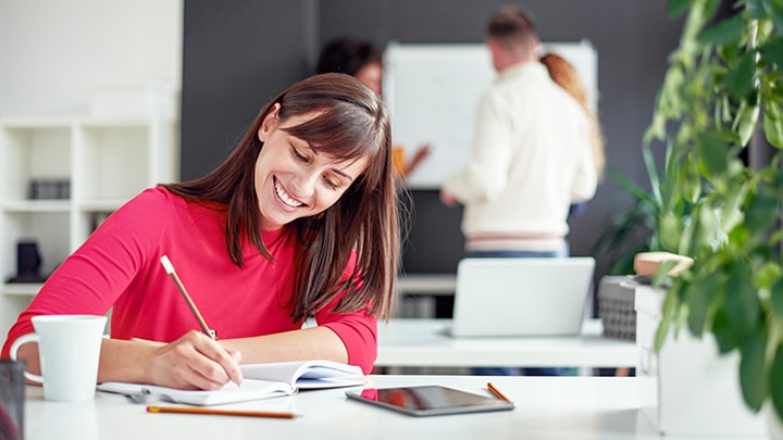 A happy woman working in an office with co-workers busy behind her