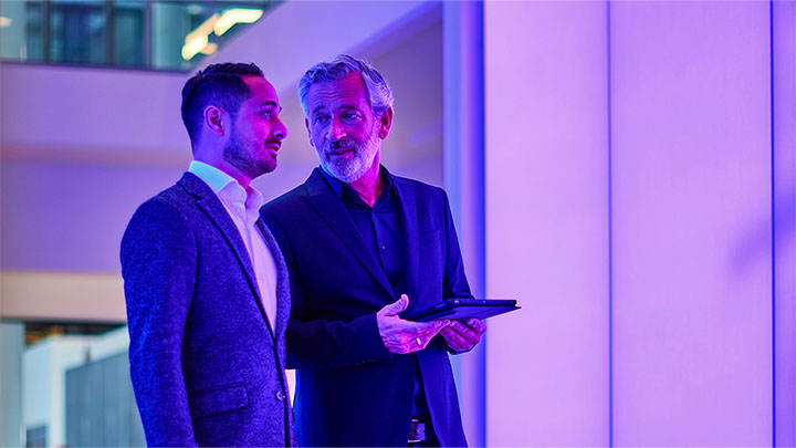 Deux collègues masculins se parlent dans un bâtiment éclairé par un éclairage violet et bleu