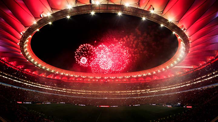 Looking up inside a large stadium to see the ceiling illuminated with red lighting and red fireworks