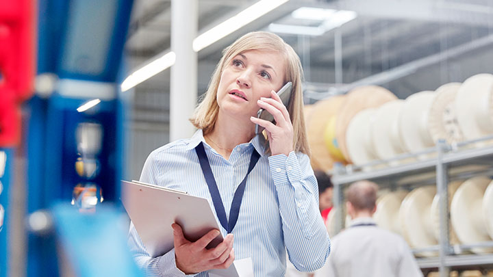 Una supervisora con una tablilla con sujetapapeles habla por el móvil en una fábrica