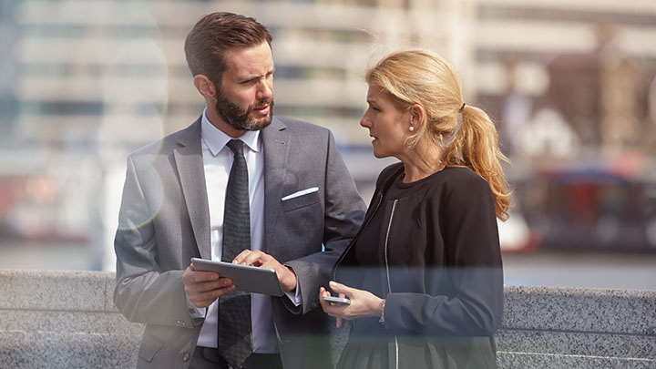 Female and male coworker discussing plans on a digital tablet outside